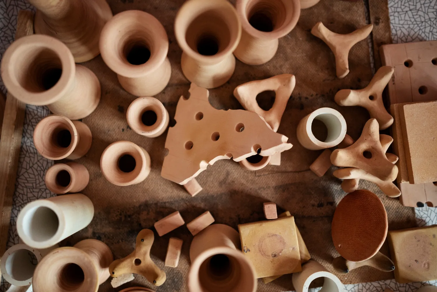 Conjunto de piezas de cerámica en diferentes formas y tamaños, incluyendo jarrones, figuras geométricas y fragmentos, sobre una superficie de tela. Ideal para la artesanía y decoración.