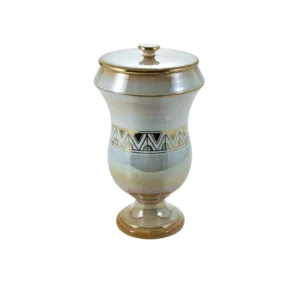 Jarrón decorativo de cerámica con tapa, presenta un diseño elegante en tonos beige y dorado, adornado con un patrón geométrico en la parte central. Ideal para decoración de interiores.