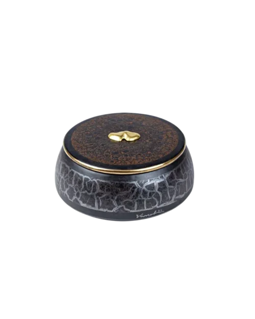 Caja decorativa de cerámica negra con un diseño agrietado y tapa marrón, adornada con un detalle dorado en forma de gota. Ideal para almacenamiento y decoración de interiores.