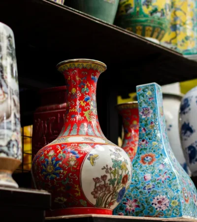 Vasos de cerámica decorativos de diferentes colores y estilos, exhibidos en una estantería. Los diseños incluyen motivos florales y escenas de la naturaleza, destacando la artesanía tradicional.